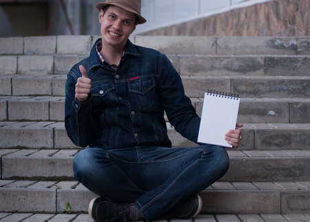 Smart young man hold notepad with mock up area for your advertising text message during preparing training project sitting with interesting literature outsideの写真素材