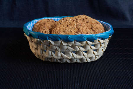 homemade oat cookies with sunflower seeds in and near blue checkered basket on black wooden backgroundの写真素材