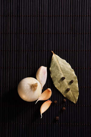 onion, garlic, black pepper and bay leaf on a black tableの写真素材