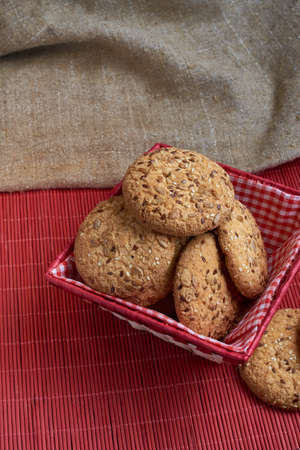 homemade oat cookies with sunflower seeds in and near red checkered basket on red wooden table
