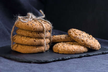 Stack of savory cookies sprinkled with sesame seeds, sunflower on shale board and two coockis