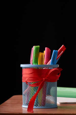 Dark wooden table with pens holder, colorful pens, notebooks. Concept education and back to school