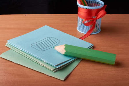 Green big pen and metal cup with crayons on desk isolated on black backgroundの写真素材