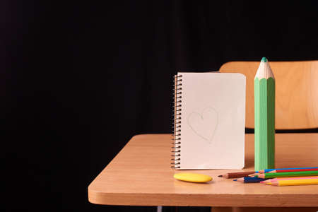 colored pencils and open notebook with big pancil on black