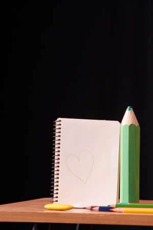 blank notebook page with colored pencils on table on black backgroundの写真素材