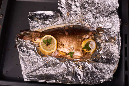 Appetizing baked fish, covered with juicy lemons, garlic and salt on side