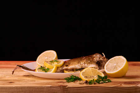 Baked fish with lemon, spices and herbs on white plate on wooden backgroundの写真素材