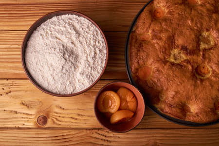 A bowl with flour and apricot cake on a wooden background on black