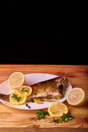 On a wooden table plate with roasted carp fish dorado with parsley, chives and lemonの写真素材