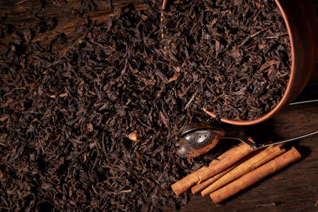 Dry tea leaves in clay bowl on black background on wooden table