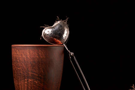 tea strainer with a cup and black tea on wooden table on dark backgroundの写真素材