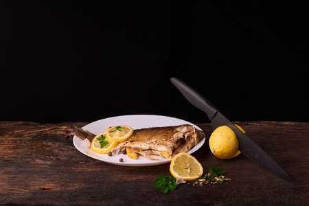 Cutted lemonwith black knife and plate with Grilled fish in the sauce and with spices and herbsの写真素材
