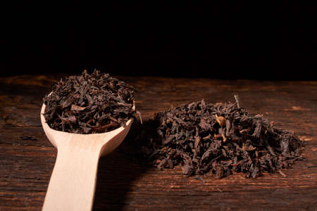 Leaves of black tea in wooden spoon on dark wooden table on blackの写真素材