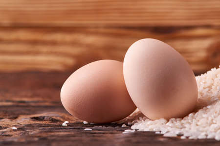 Bunch of rice and uncooced eggs on wooden tableの写真素材