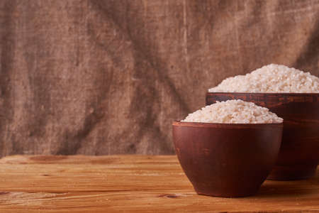 White rice in clay bowl on wooden table and sacking backgroundの写真素材