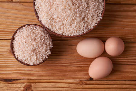 White rice in clay bowl on table and eggs on wood background