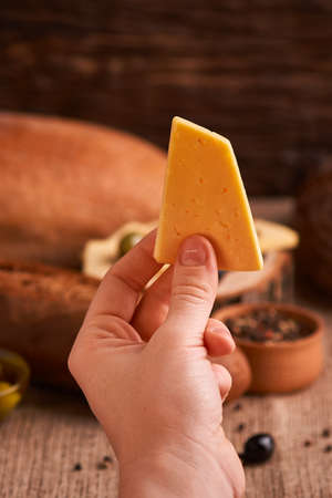 Woman hold slice of Traditional Dutch semi hard cheese on Olives, bread and baguette backgroundの写真素材