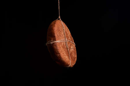 Round fresh bread hanging on a rope on a black background.