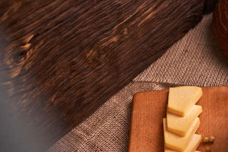 Slices of cheese on wooden desk near baguette and milk