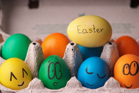 Colorful Easter eggs with painted face in egg carton box on wooden backgroundの写真素材