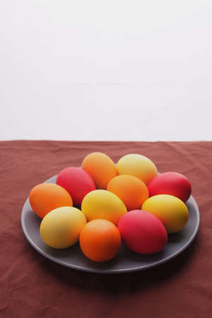 on table is plate with colored eggs on white background. Yellow, orange and red eggs