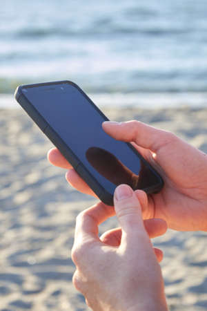 Mockup image of a woman's hands holding a mobile phone on the beachの写真素材