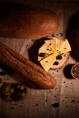 Traditional Dutch semi hard cheese served with olives on rural table with sacking