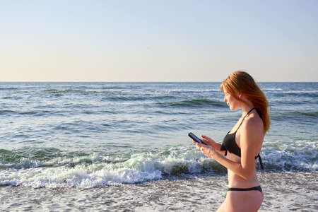 Cute smiling girl texting with her mobile phone message on a beachの写真素材