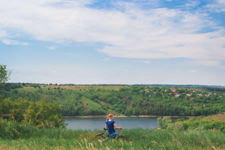 Girl with a bicycle on the river shore. A girl sits on a bicycle near a tent on the bike.