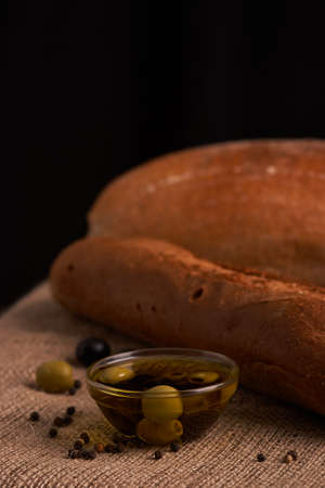 fresh bread baguette with olive oil, olives. cheese and rosemary on wooden backgroundの写真素材