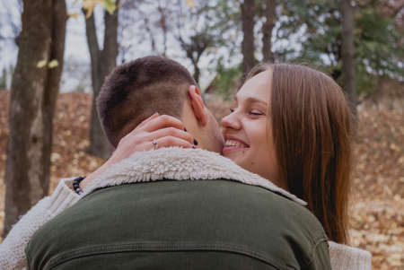 Couple in love stand on autumn fallen leaves in a park, enjoying a beautiful autumn day