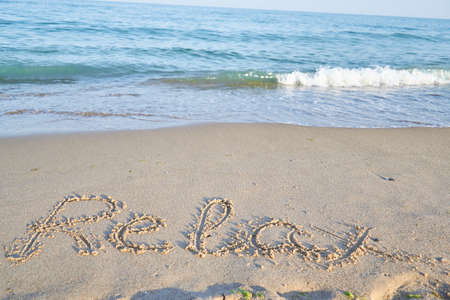 relax word is written on the beach sand with waterの写真素材