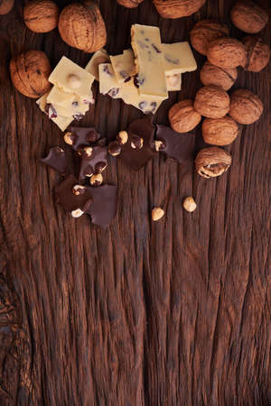 Nuts and milk and dark chocolate pieces on wooden background. Tasty and sweet foodの写真素材