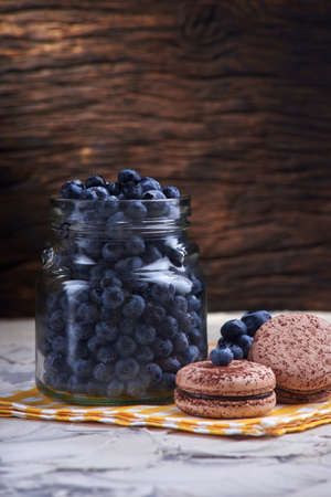 Fresh and tasty blueberry berries in a glass jar with sweet macaroons on a checkered napkinの写真素材