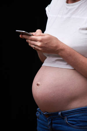 upset pregnant woman with phone in her hands. technology and pregnancy. pregnancy, motherhood, technology, people and expectation concept - sad pregnant woman calling on smartphone at homeの写真素材