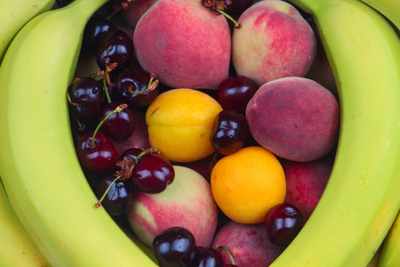 A Wooden Bowl of Fruits on a Wooden Background, Banana, Cherries, Peaches.の写真素材
