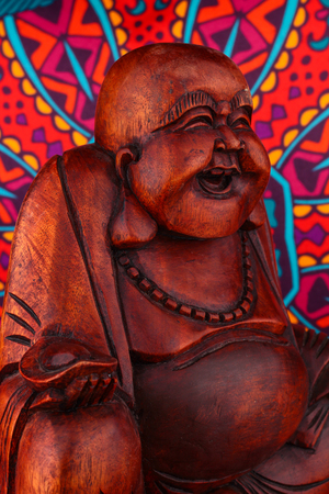 Buddha statue on a colorful background / featuring a wooden statue of  cheerful wise Buddha on colorful Oriental artistic pattern backgroundの写真素材
