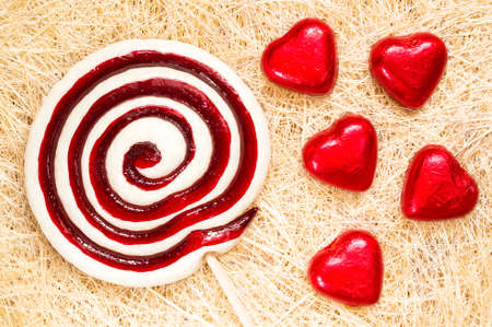 A retro looking photo of lollipop and heart shaped candies on a straw background.の写真素材