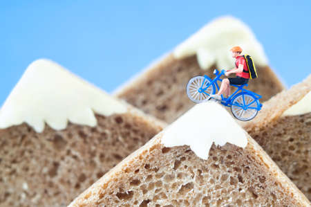 A toy cyclist is taking a ride on the mountains, made of healthy rye bread and creamy cheese. Ecotourism and healthy eating concept.の写真素材