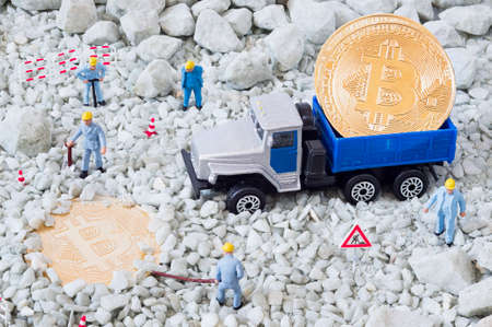 A photo of toy workers, bitcoins, a toy truck and a road sign. Bitcoin mining, blockchain concept.の写真素材