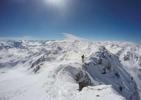 Man with yellow jacket climbing a mountain on a ridge with snow in winter in Austriaの写真素材