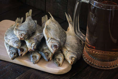Dried fish on a wooden board and a mug of beer on a wooden background. The concept of recreation, meetings.の写真素材