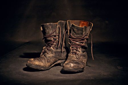 old soldier's boots worn with scratches and untied shoelaces on white backgroundの写真素材