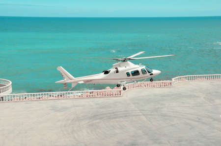 white helicopter lands on a helipad near the sea. Helicopter takeoff.
