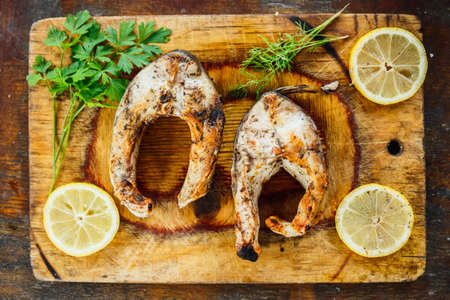 pieces of grilled fish, parsley and lemon on a wooden boardの写真素材
