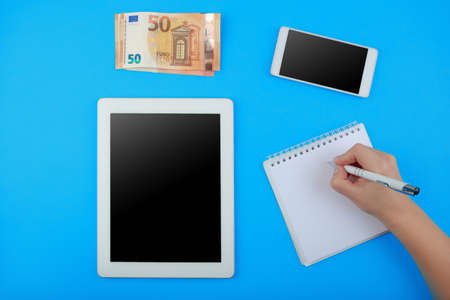 top view on the tablet, Notepad with pen, phone and Euro banknotes on blue background
