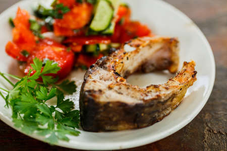 grilled or fried piece of fish and salad on a white plate on wooden tableの写真素材