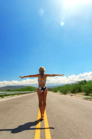 girl in bikini back view walking on asphalt road in sunny day. Travel concept, way to paradiseの写真素材