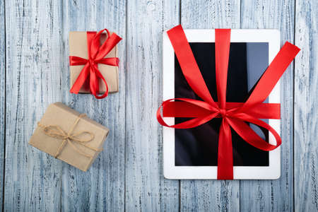 gifts and a tablet on a white old wooden background wrapped in red ribbonの写真素材