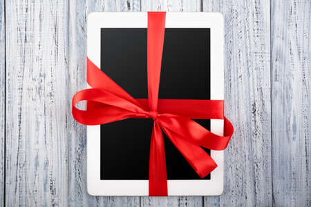 tablet wrapped in a red ribbon on a vintage white wooden background. holidaysの写真素材
